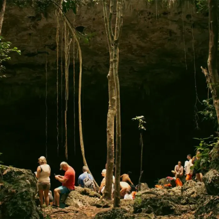 a group of people in a cenote entrance in a jungle tour resting after a buggy adventure