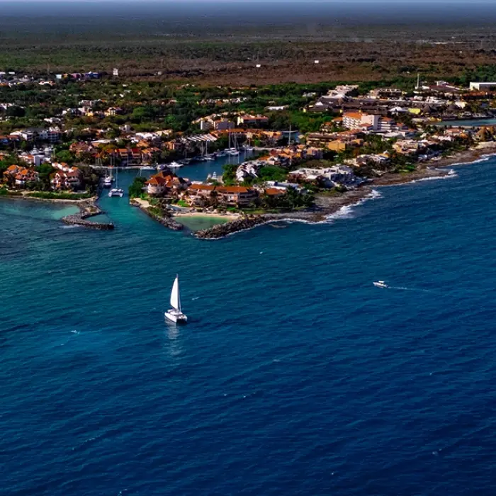 Aerial view of a coastal town with turquoise waters and a sailboat in the distance