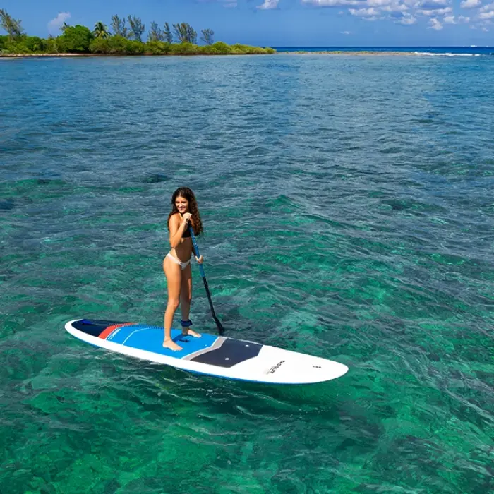 Woman paddleboarding on calm, transparent waters surrounded by nature