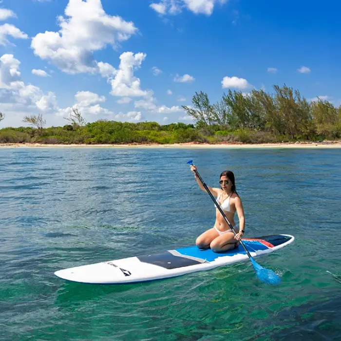 Woman sitting on a paddleboard, raising her hand in the middle of the sea