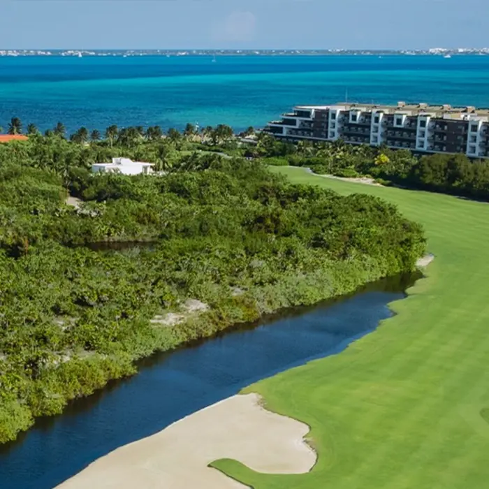 Expansive aerial view of the Greg Norman signature fairways winding through lush mangroves next to a luxury resort and the Caribbean Sea