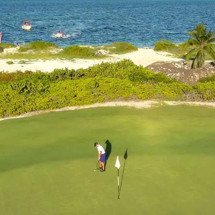 A happy couple smiling while driving a golf cart past the modern clubhouse facilities before their round at Playa Mujeres Golf Club