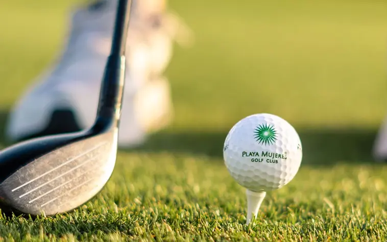 A close-up of a branded Playa Mujeres Golf Club ball on a tee ready for a drive on the pristine championship course