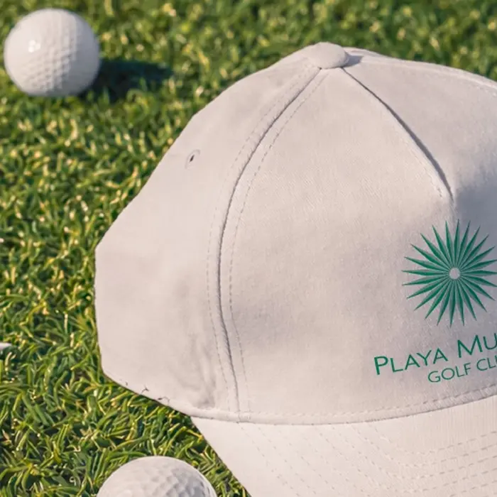 A close-up of a branded Playa Mujeres Golf Club cap resting on the pristine practice green before a championship round