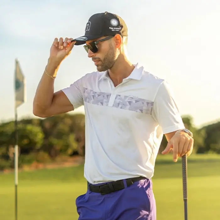 A golfer in premium attire adjusts his cap while enjoying a sunset round at the luxury Greg Norman-designed golf course