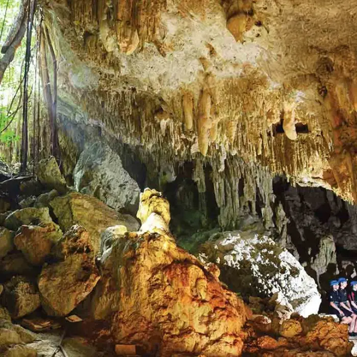 Rio Secreto cave entrance: Group of people sitting at the entrance of a large, illuminated cave with hanging stalactites