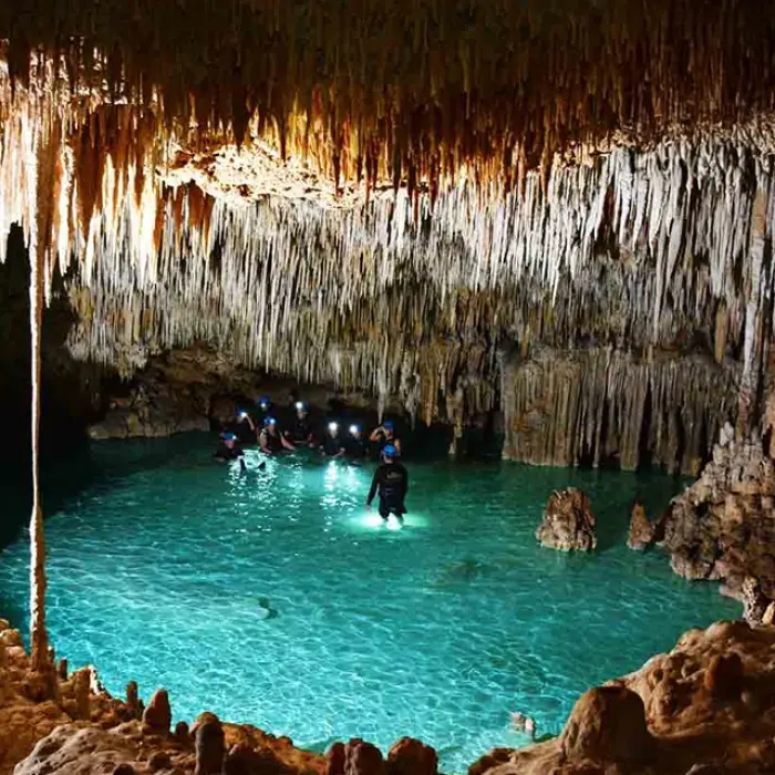 Rio Secreto cave exploration group: Group of people with headlamps exploring the clear turquoise water and impressive stalactites inside Rio Secreto