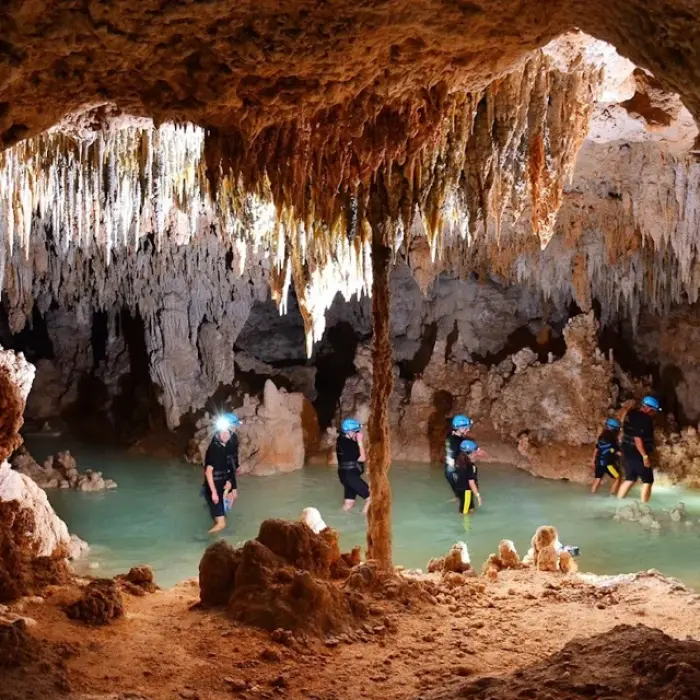 Rio Secreto cave walk: Group of explorers with headlamps walking through the shallow, clear water inside a Rio Secreto cave filled with unique rock formations