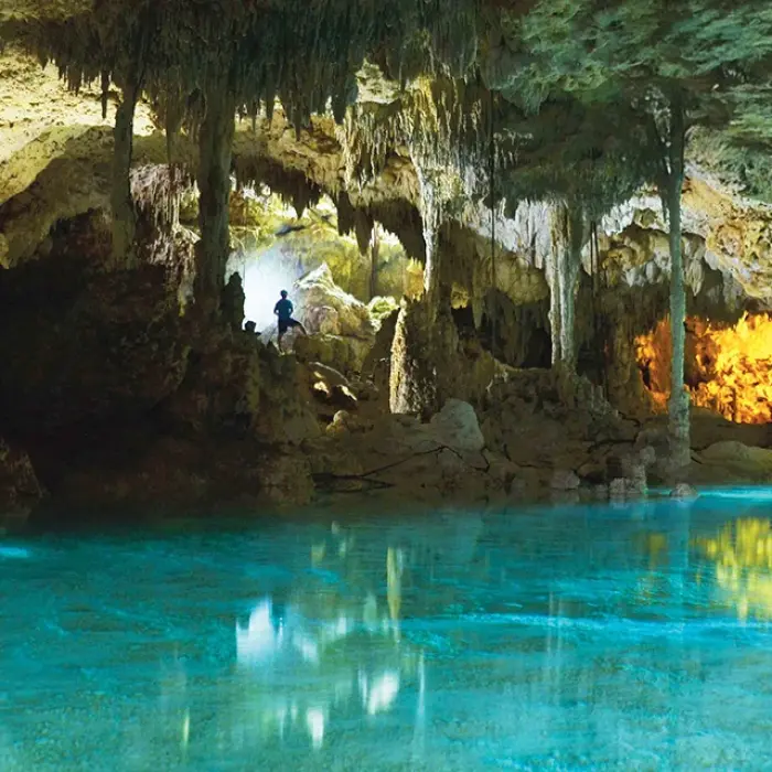 Rio Secreto exploration: Turquoise water inside a cave with rock formations and a person in the distance