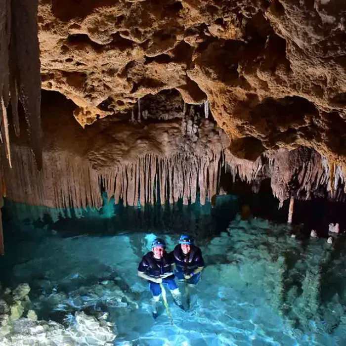 Rio Secreto cenote swim: Two people swimming in the crystal-clear turquoise water of an underground cenote at Rio Secreto, surrounded by impressive rock formations