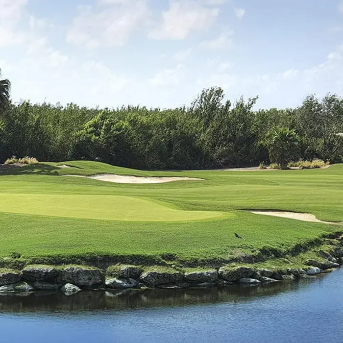 A scenic view across a tranquil natural water hazard towards a manicured fairway and sand bunkers, with thick jungle in the background at Riviera Cancún Golf Club