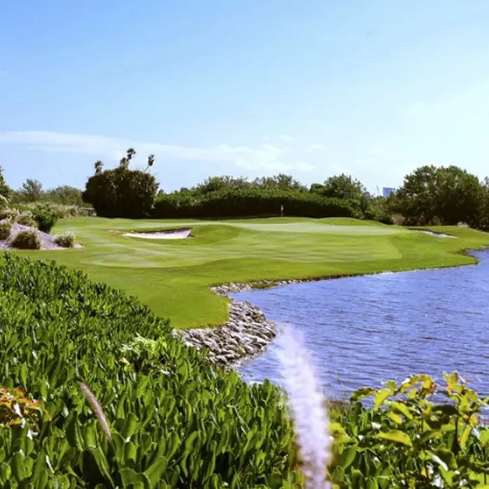 A sweeping, flawless fairway curving gracefully alongside a vibrant blue lake and native coastal grasses at Riviera Cancún