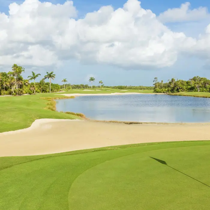 A view from behind the green at Riviera Cancún Golf Club, looking back over a large sand bunker and an expansive lake towards the tropical jungle in the distance