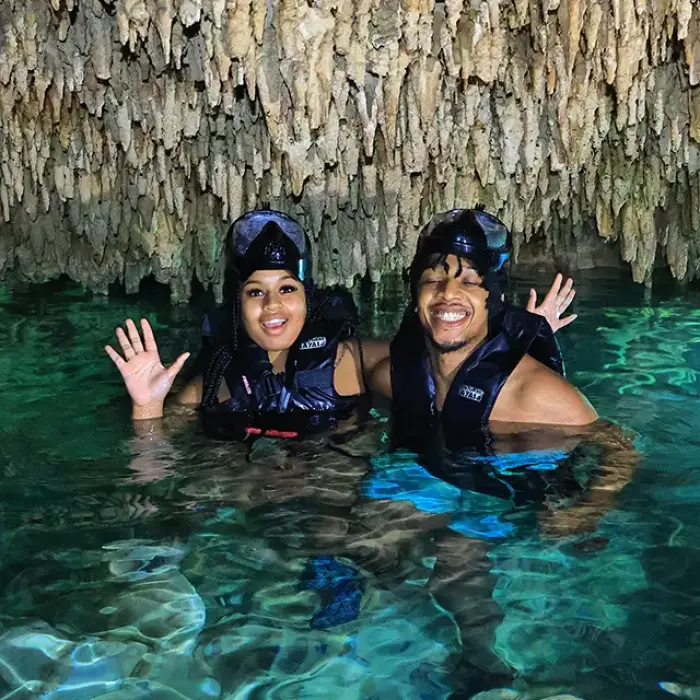 Happy couple smiling inside a cenote cave with stalactites, swimming in fresh blue water