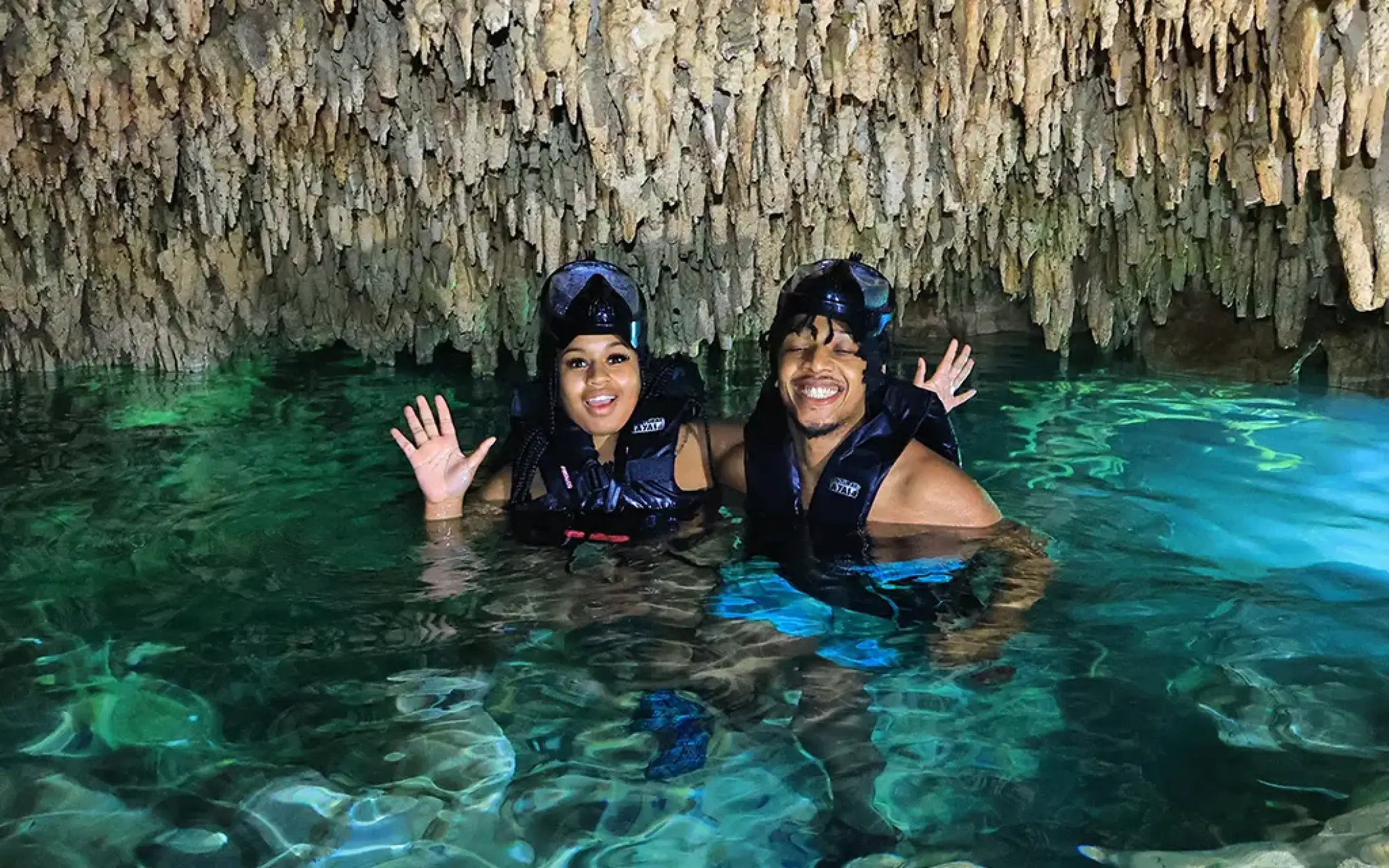 Happy couple smiling inside a cenote cave with stalactites, swimming in fresh blue water