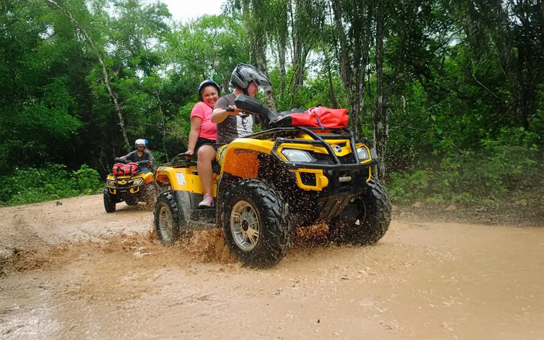 Couple riding a yellow ATV through a muddy trail on a jungle adventure tour