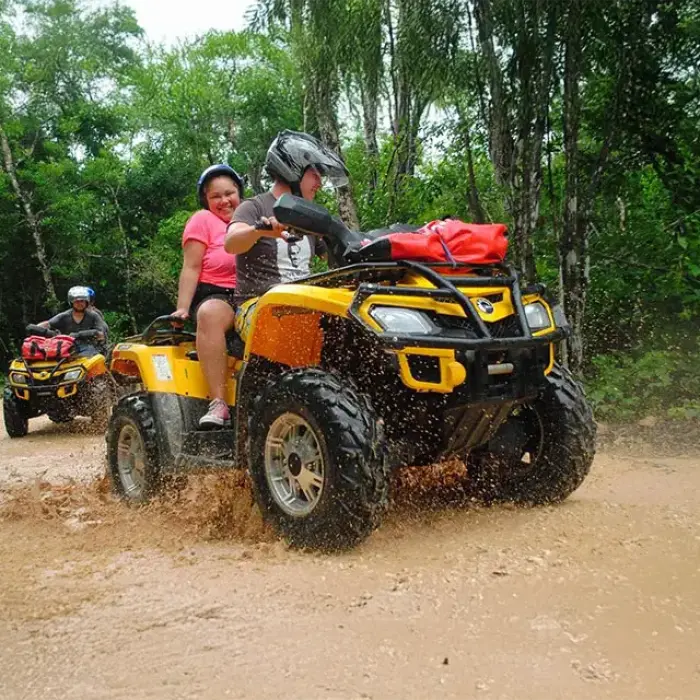 Couple riding a yellow ATV through a muddy trail on a jungle adventure tour