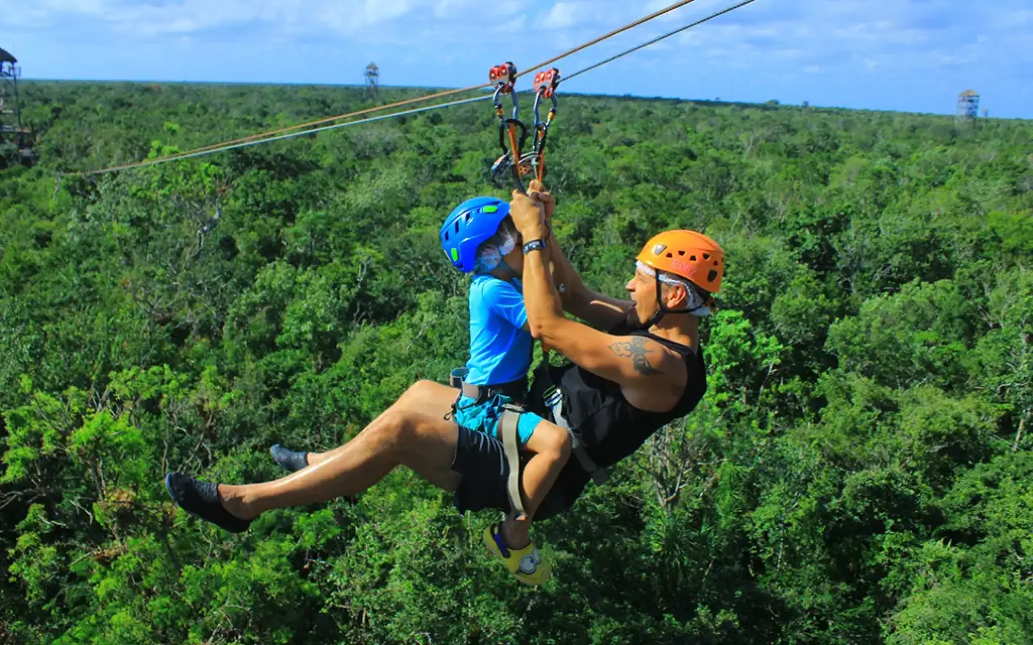 Father and child tandem ziplining over lush green jungle scenery in Mexico