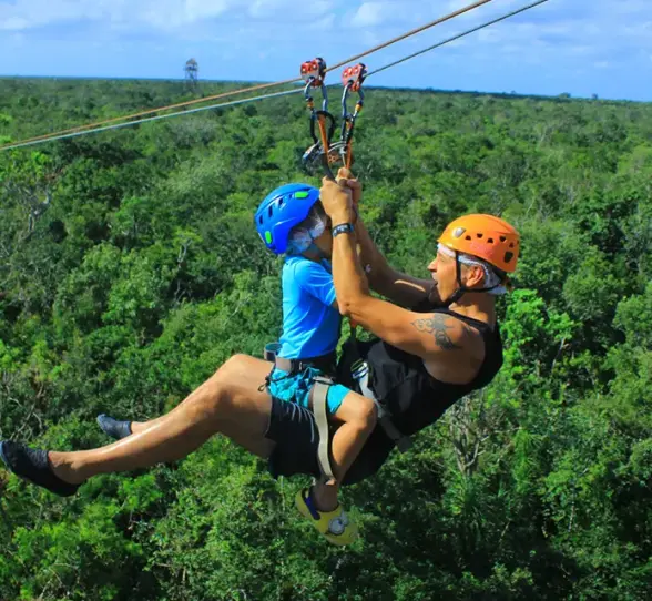 Father and child tandem ziplining over lush green jungle scenery in Mexico