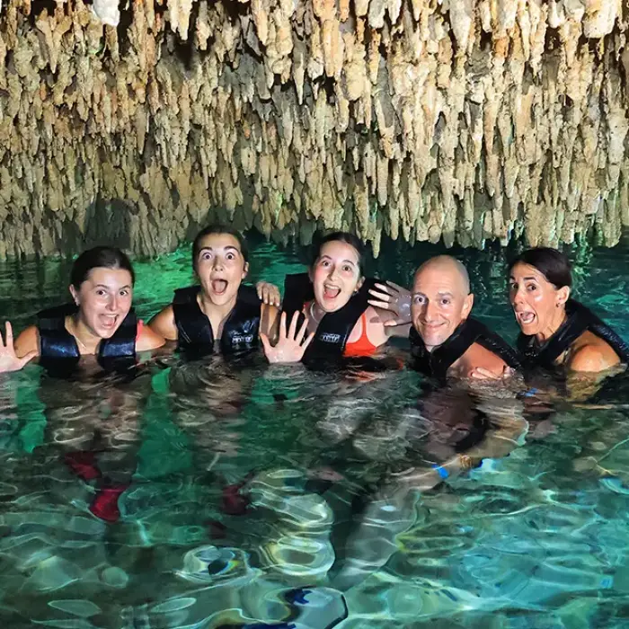 Group of friends swimming in a cenote cave with stalactites overhead in Riviera Maya