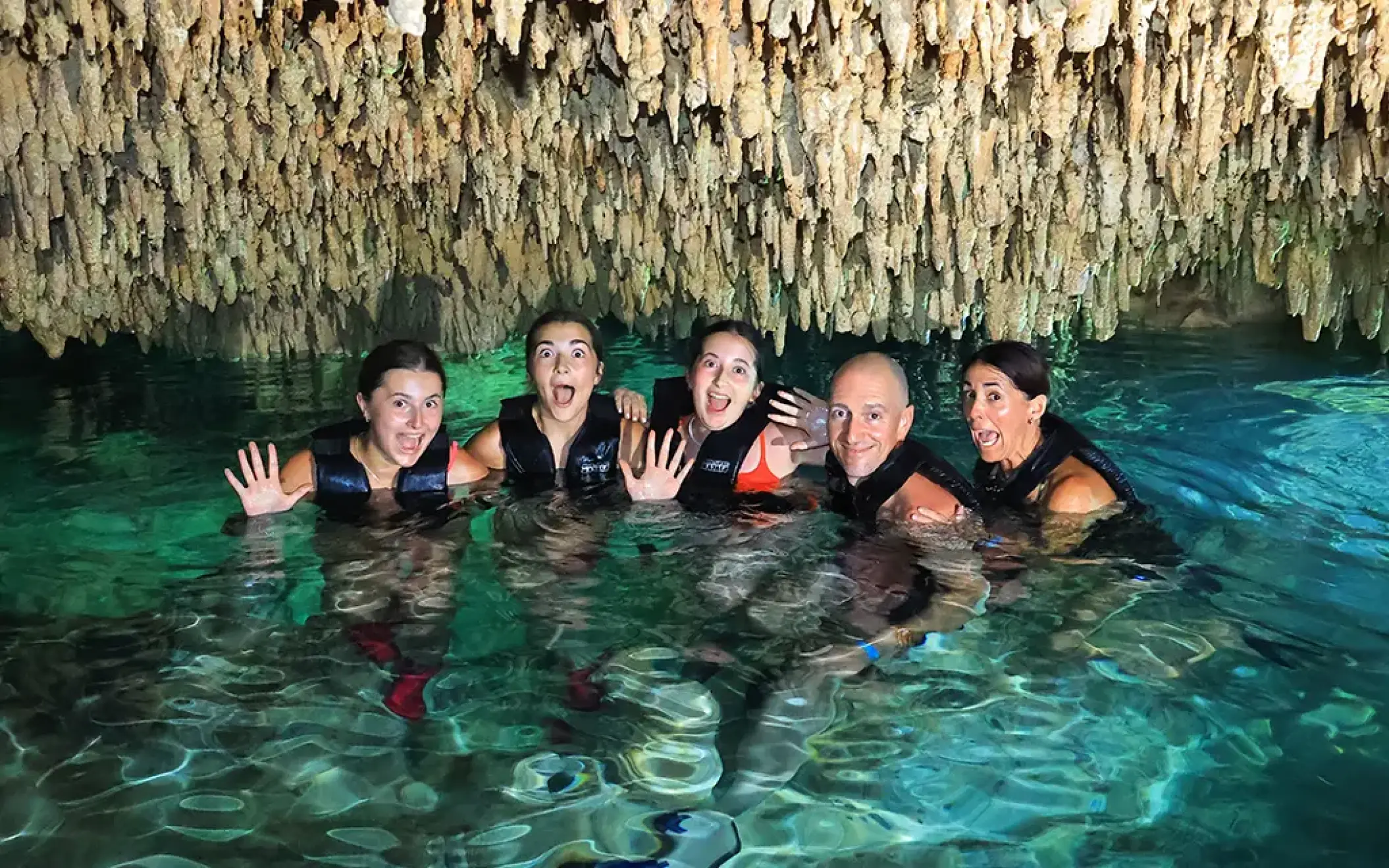 Group of friends swimming in a cenote cave with stalactites overhead in Riviera Maya