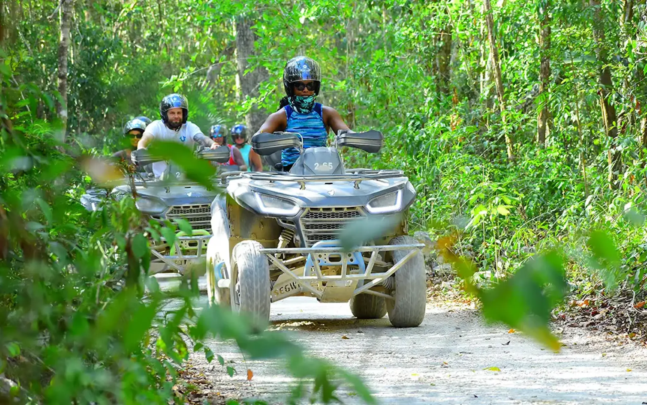 Adventure group riding white ATVs along a dirt road in the jungle