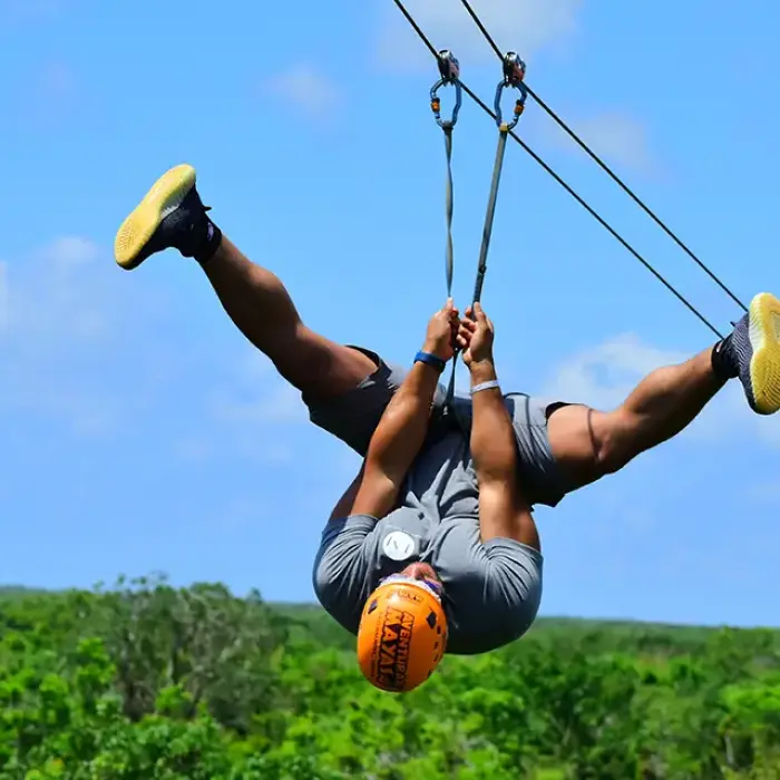 Tourist upside down ziplining above the jungle with a blue sky background