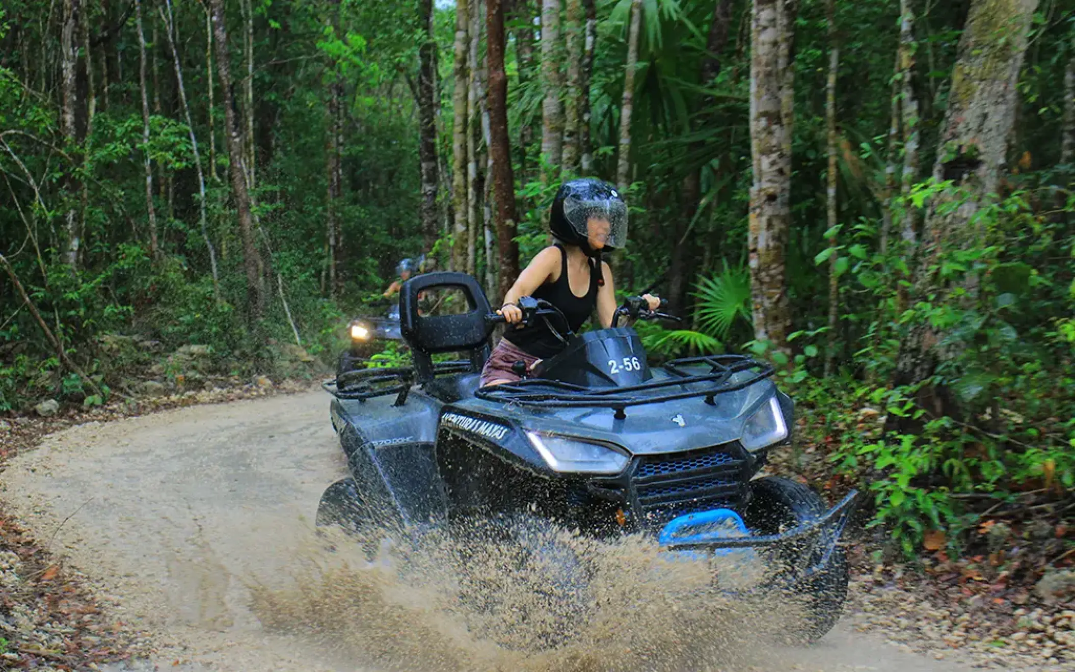 Woman riding an ATV through a splash of water on an adventurous jungle ride