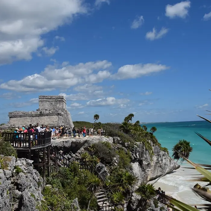 The Mayan ruins of Tulum perched on a cliff overlooking the Caribbean Sea, with tourists exploring the site