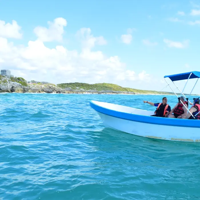 A group of tourists on a boat tour with the Tulum ruins visible in the background