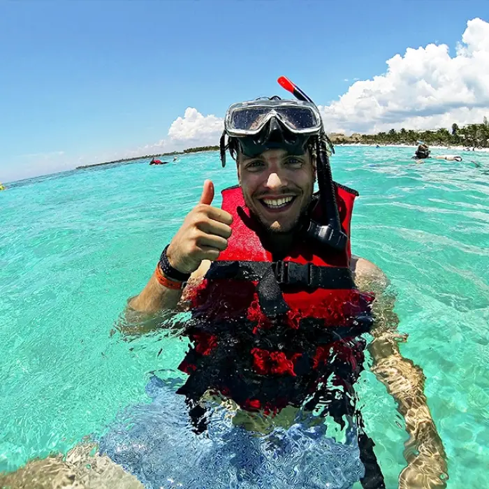 Man wearing a snorkel and life jacket, giving a thumbs-up in crystal-clear waters