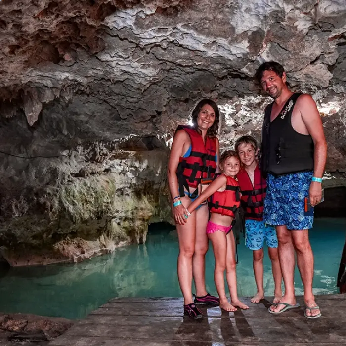 Family posing at a cenote entrance with rock formations in the background