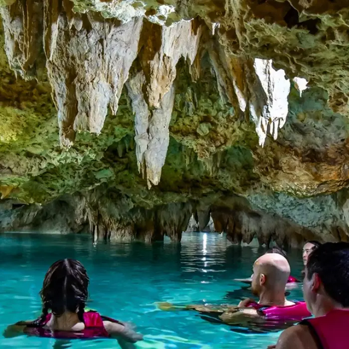 Tourists swimming inside a cenote with stalactites hanging from the cave ceiling