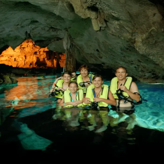 Family adventure inside a peaceful cenote cave, wearing life jackets and enjoying the beauty of nature
