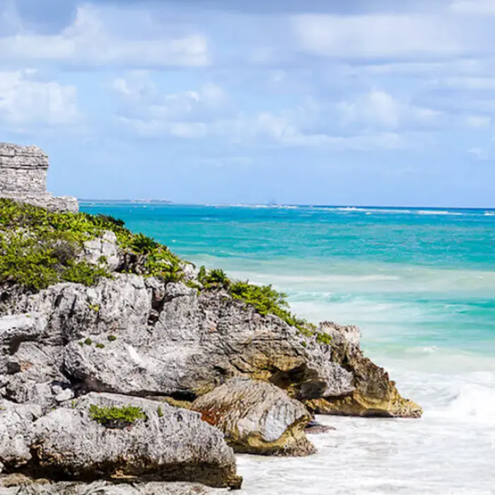 A small Mayan temple perched dramatically on the rocky cliffs overlooking the turquoise ocean