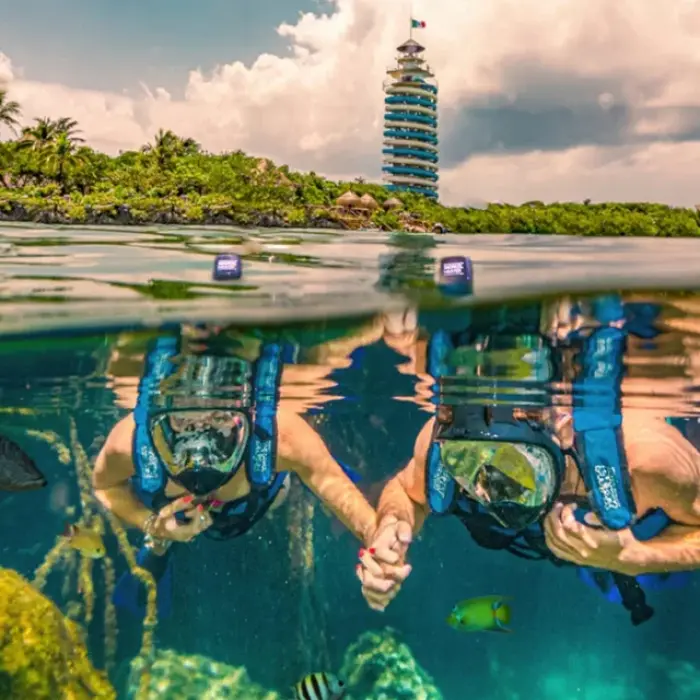 Couple holding hands underwater while snorkeling near the lighthouse at Xel-Há
