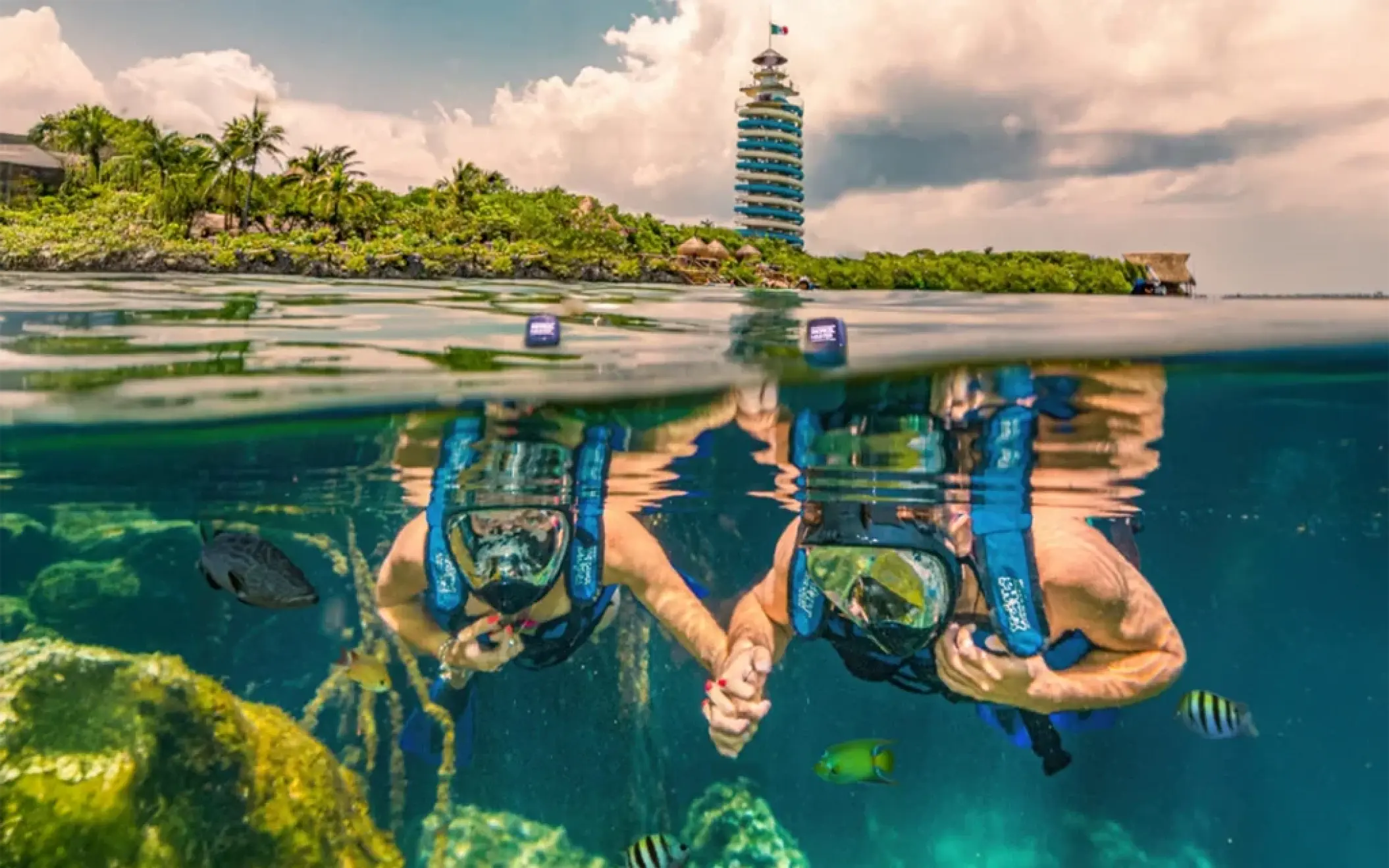 Couple holding hands underwater while snorkeling near the lighthouse at Xel-Há