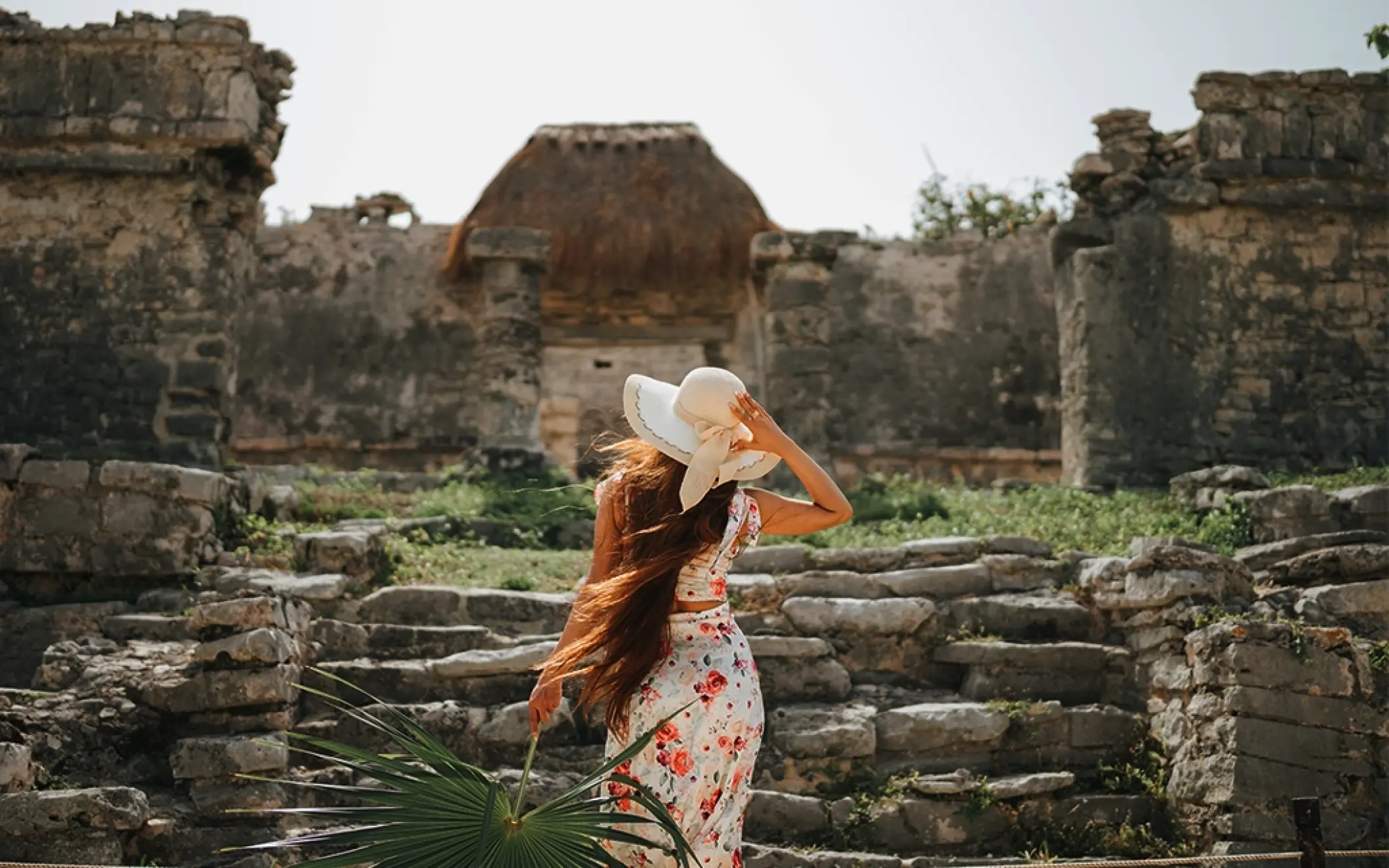 Woman in a sunhat exploring the ancient stone steps of the Tulum archaeological site