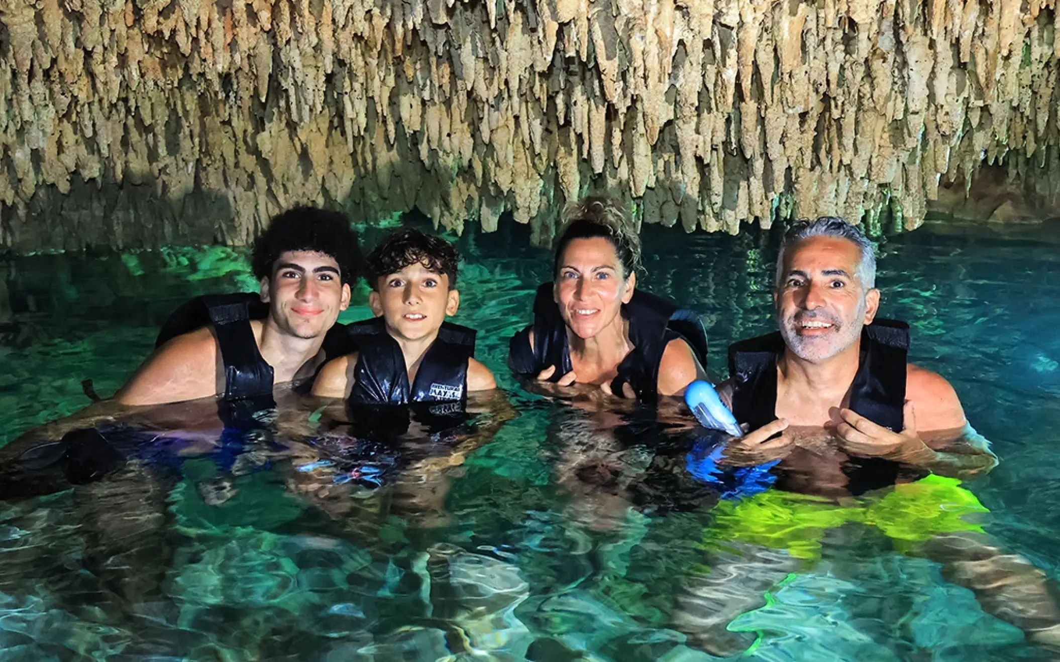 Family floating inside a cenote cave under stalactites, enjoying the cool waters