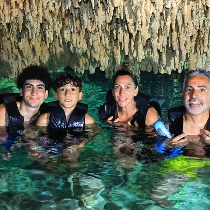 Family floating inside a cenote cave under stalactites, enjoying the cool waters