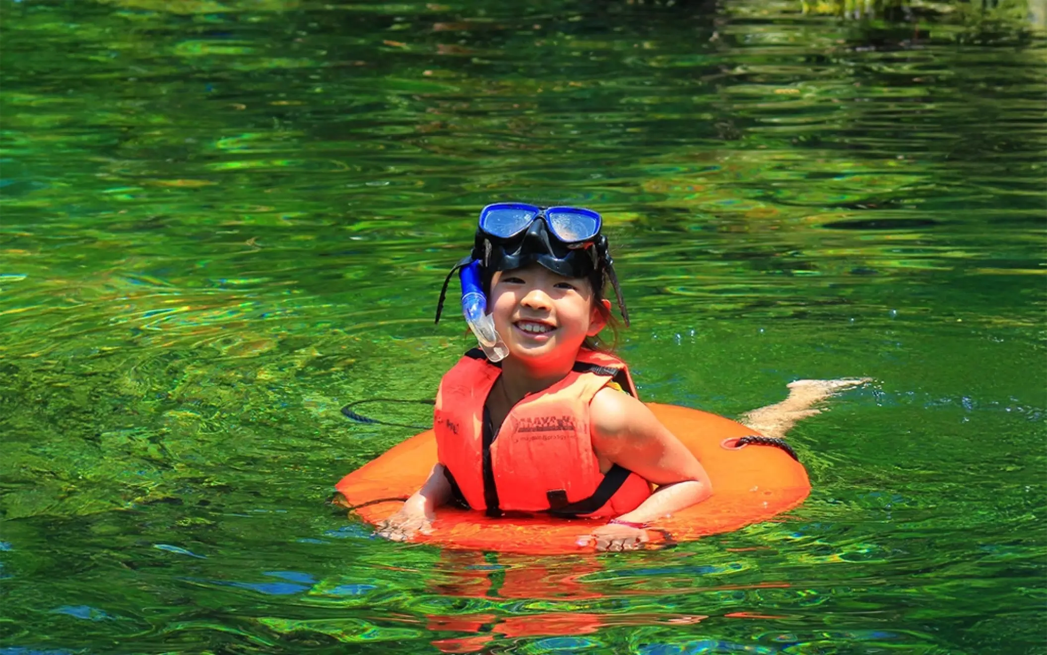 Child smiling while floating with a life vest in the calm, clear waters of Xel-Há