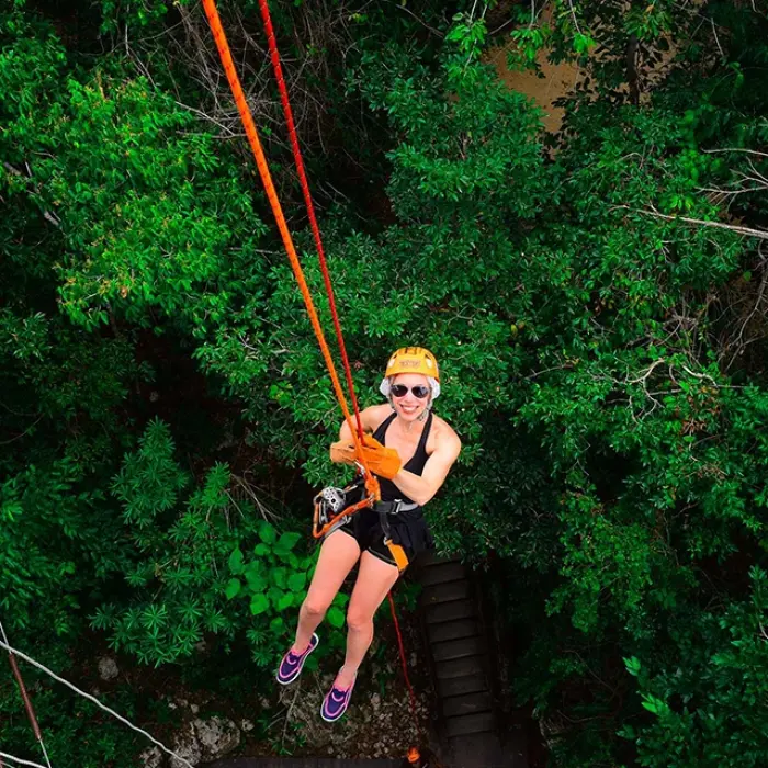 Woman dangling mid-air during an adrenaline-pumping jungle rappel experience at Xel-Há