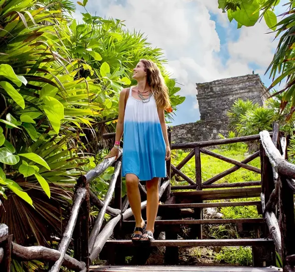 Woman walking down wooden steps surrounded by lush greenery at Tulum. Nature escape!