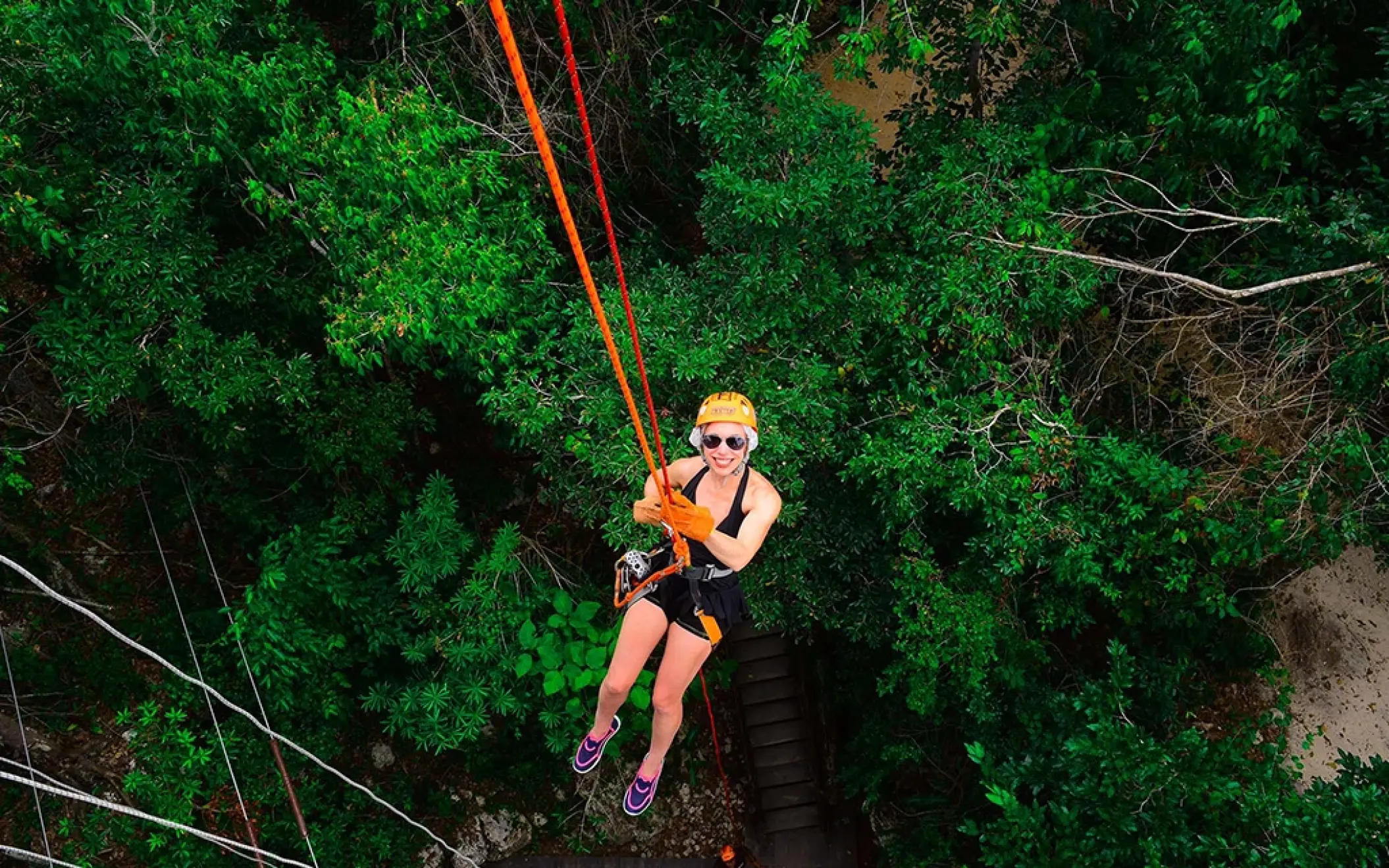 Side view of a person sliding down a zipline through the Tulum jungle, part of the Tulum Xtreme Tour