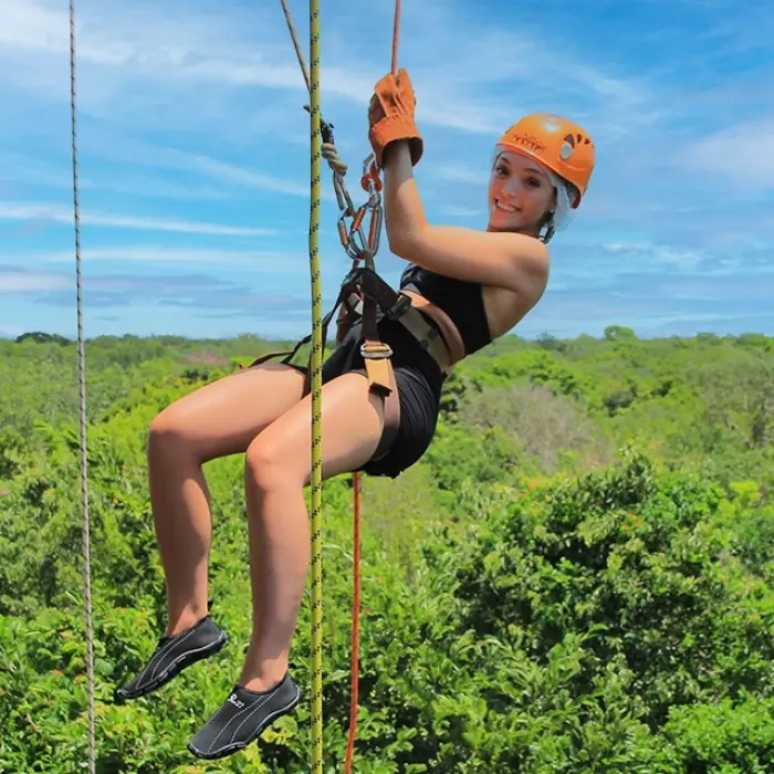 Adventurer using a rope to rappel down a jungle cliff on the Tulum Xtreme Tour