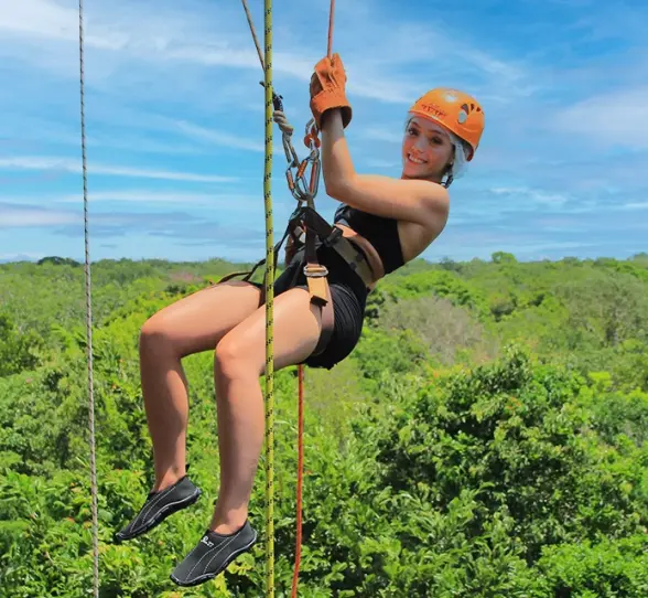 Adventurer using a rope to rappel down a jungle cliff on the Tulum Xtreme Tour
