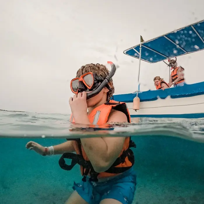 Akumal snorkeling prep: Boy with snorkel mask and life vest in the water near a boat in Akumal