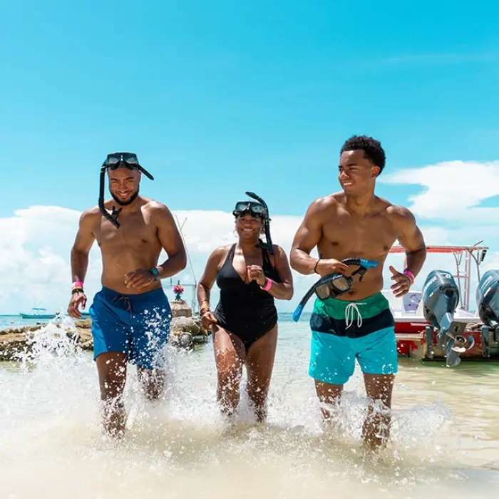 Akumal snorkeling fun: Three friends running into the clear turquoise water of Akumal with snorkel gear