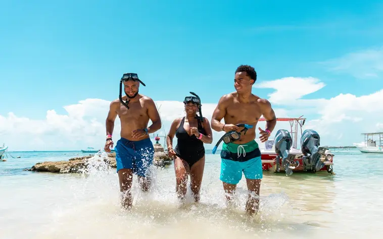 Akumal snorkeling fun: Three friends running into the clear turquoise water of Akumal with snorkel gear