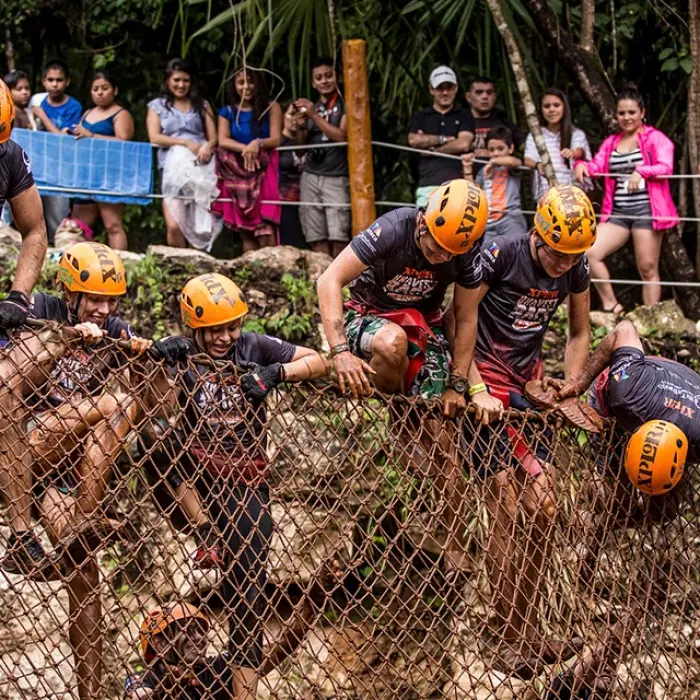 Group crawling through a muddy ropes course with helmets